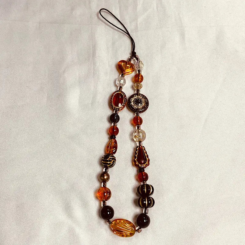 A beaded phone charm strap with an anti-lost lanyard featuring amber, brown, and clear glass beads.