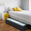 A bed with a mattress and bedding, featuring a black under bed storage organizer bin.