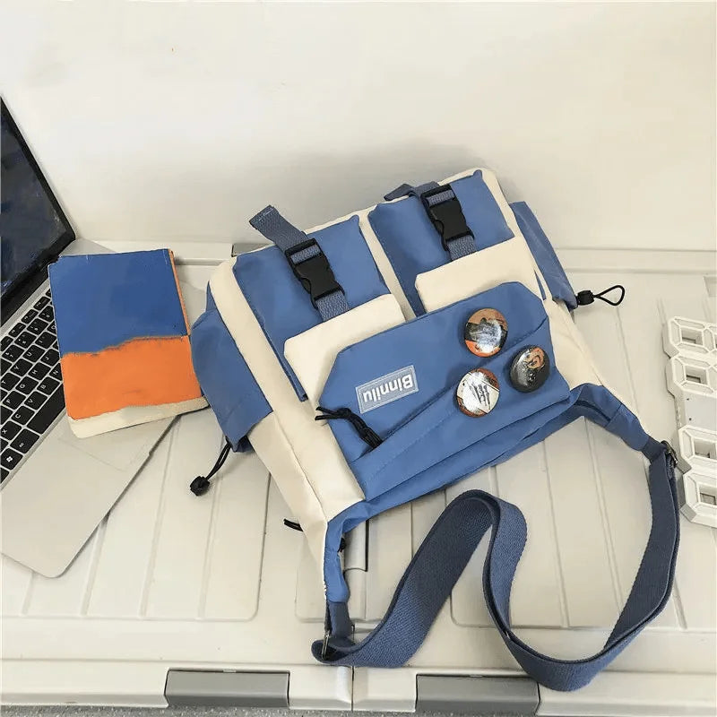 Bolso cruz de nylon azul y beige con correas negras sobre un escritorio blanco junto a una computadora portátil.
