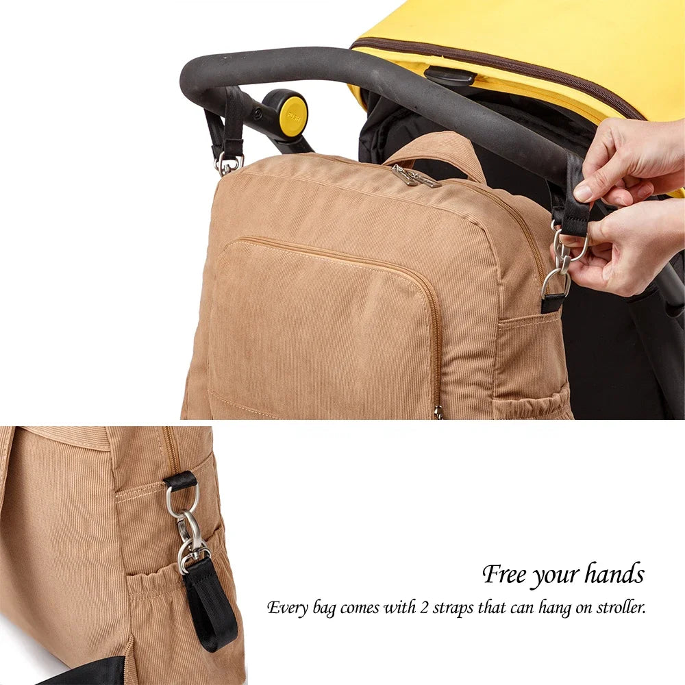 A close-up of a tan soft corduroy diaper backpack with black straps being attached to a stroller.