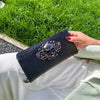 A hand holds a black leather wallet with silver skull embellishments against a bright green grassy background.