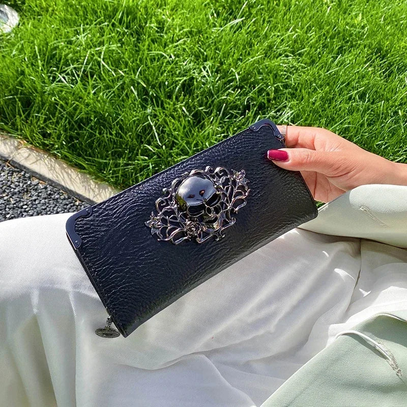A hand holds a black leather wallet with silver skull embellishments against a bright green grassy background.