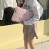 A person holds a pink quilted slim laptop sleeve for a MacBook or tablet outside.