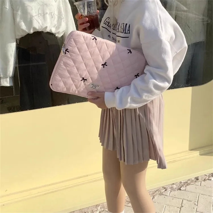 A person holds a pink quilted slim laptop sleeve for a MacBook or tablet outside.