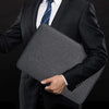 A person wearing a dark suit holds a gray waterproof canvas laptop sleeve with a soft fleece lining.