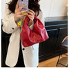 A woman holds a red leather crossbody tote bag and a patterned card in a light blazer indoors.