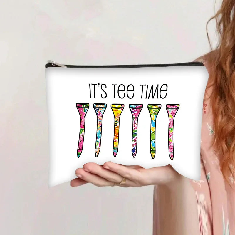 Una mano sostiene una bolsa de almacenamiento cosmético blanca con el texto "It's tee time" impreso, con formas coloridas de 