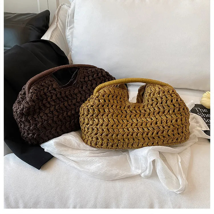 A close-up of a brown straw woven tote handbag resting on white fabric and bedding.