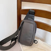 A dark gray chest bag with a black strap is resting on a wooden chair and a white cloth.