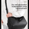 A person wearing a white jacket holds a black waterproof travel duffle bag with a separate shoe compartment.