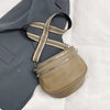 A tan soft leather crossbody bag with a striped adjustable strap is shown next to a gray blazer.