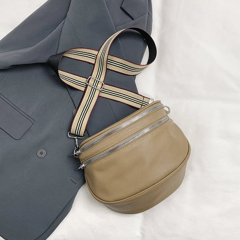 A tan soft leather crossbody bag with a striped adjustable strap is shown next to a gray blazer.