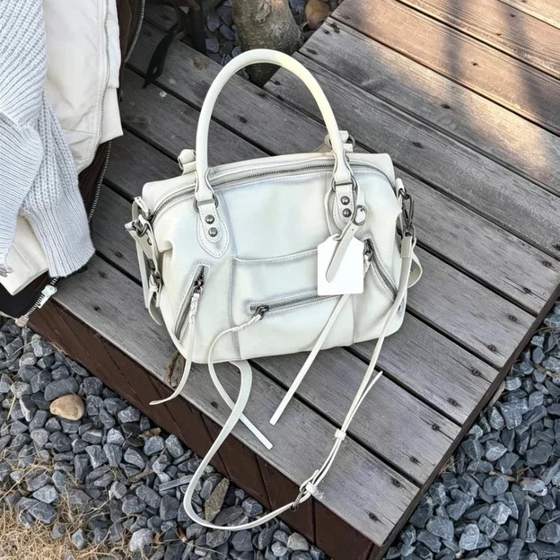 A cream vintage PU leather crossbody tote bag with a white adjustable strap resting on a wooden surface.