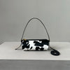 A black and white cow print cylinder shoulder bag with a thin black strap resting on a light gray surface.