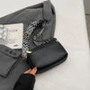A woman's hand is holding a black vegan PU crossbody bag with a patterned gold chain strap, next to a gray blazer.