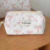 A white quilted cosmetic bag with pink ribbon embroidery rests on a wooden surface.
