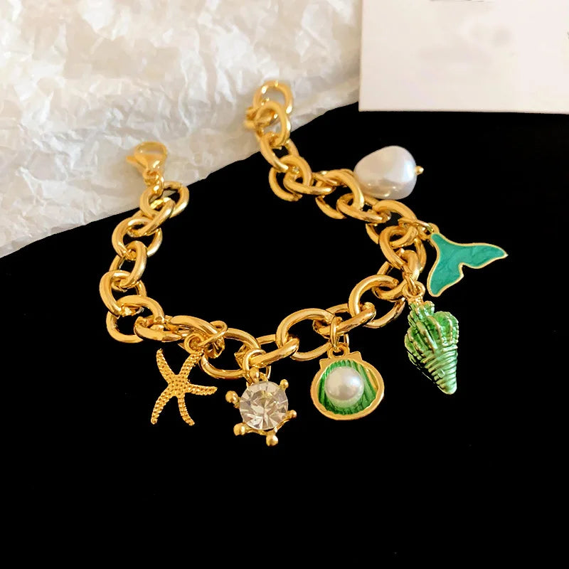 Gold chain bracelet featuring an ocean pearl, starfish, and green leaf charms.