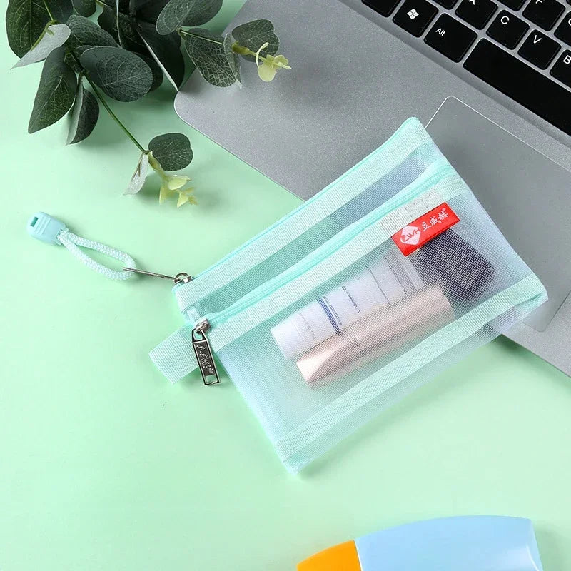 A light mint green zipper pouch containing a pink cosmetic product and a small card, placed on a laptop beside green leaves.