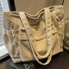 Sac en corduroy beige clair avec plusieurs poches et une sangle, exposé sur une surface sombre.