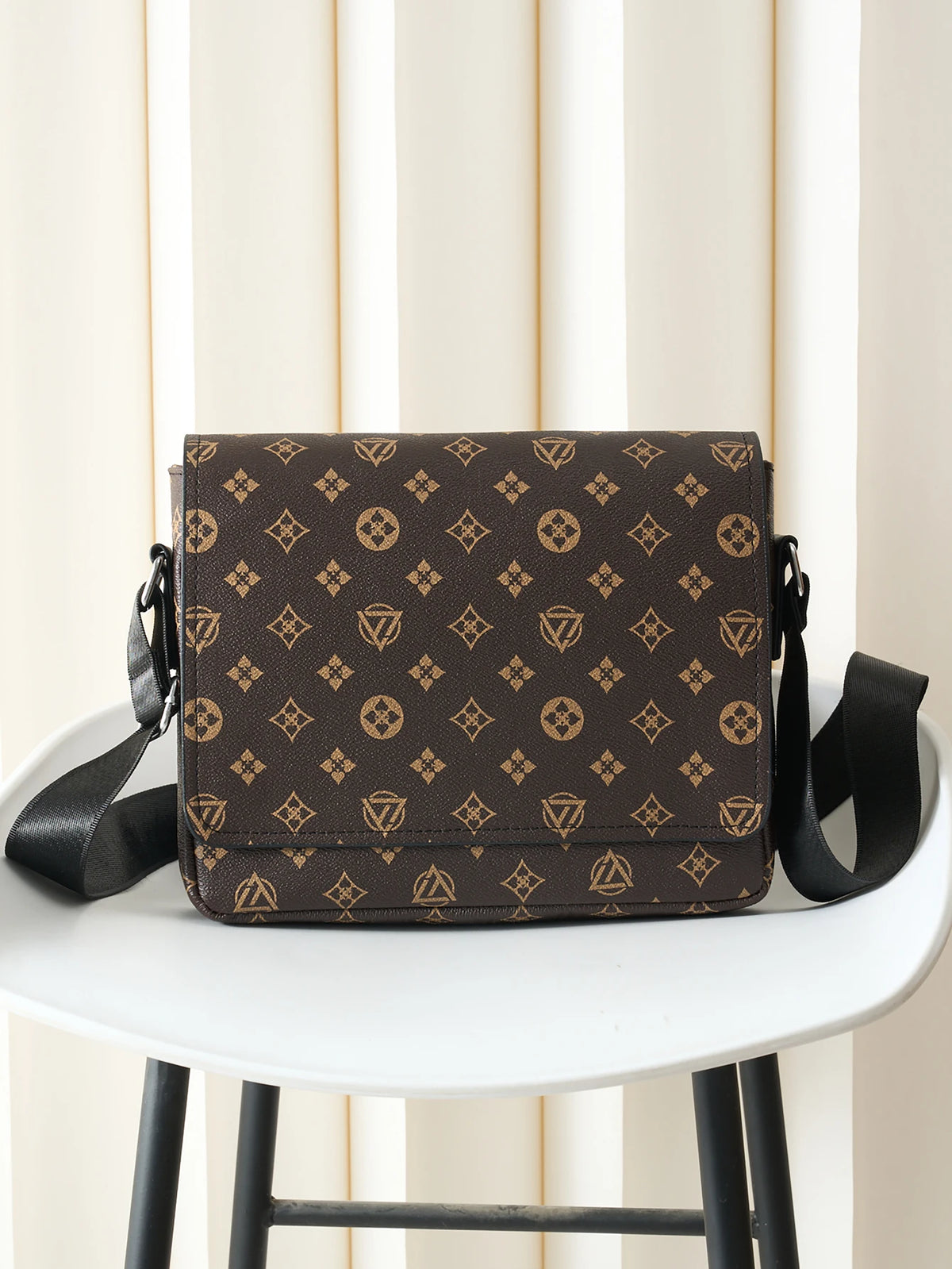 A brown men's casual crossbody bag with an easy flap design resting on a white table.