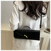 A black crocodile-embossed clutch bag is held by a person wearing a white top.