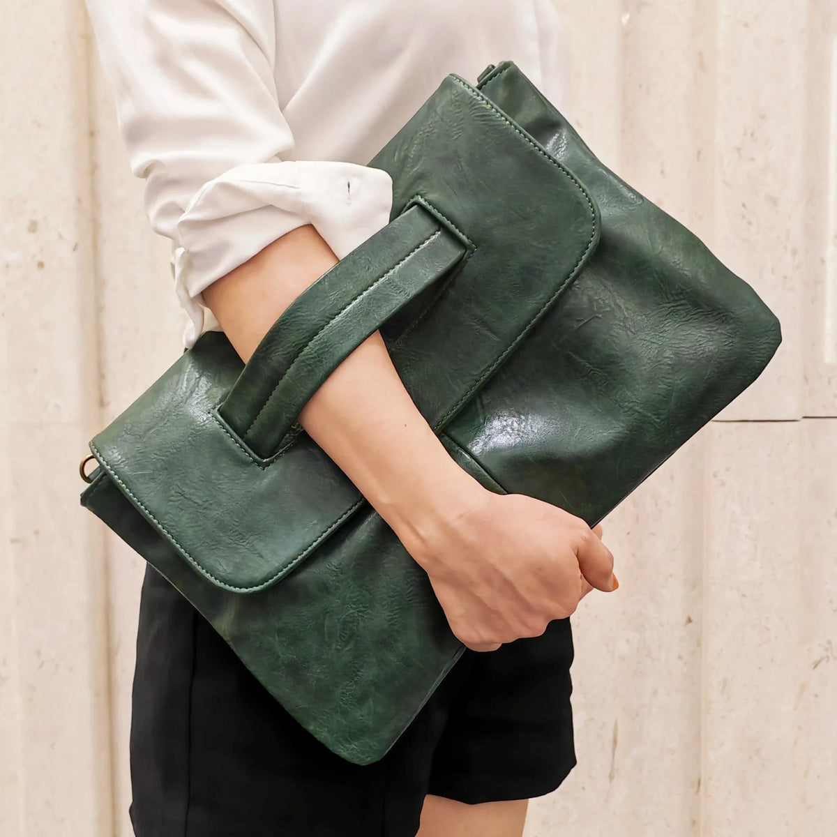 A close-up of an elegant dark green sequined crossbody clutch bag being held by a person wearing a white shirt and black shor