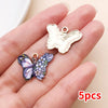 A hand holds a set of five gold-toned butterfly enamel charms.