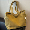A mustard yellow corduroy handbag with vertical ribbing and a drawstring closure is displayed on a dark surface.