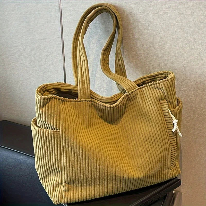 A mustard yellow corduroy handbag with vertical ribbing and a drawstring closure is displayed on a dark surface.
