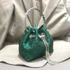 A dark green crystal-embellished evening clutch with a silver chain strap resting on a light fabric surface.