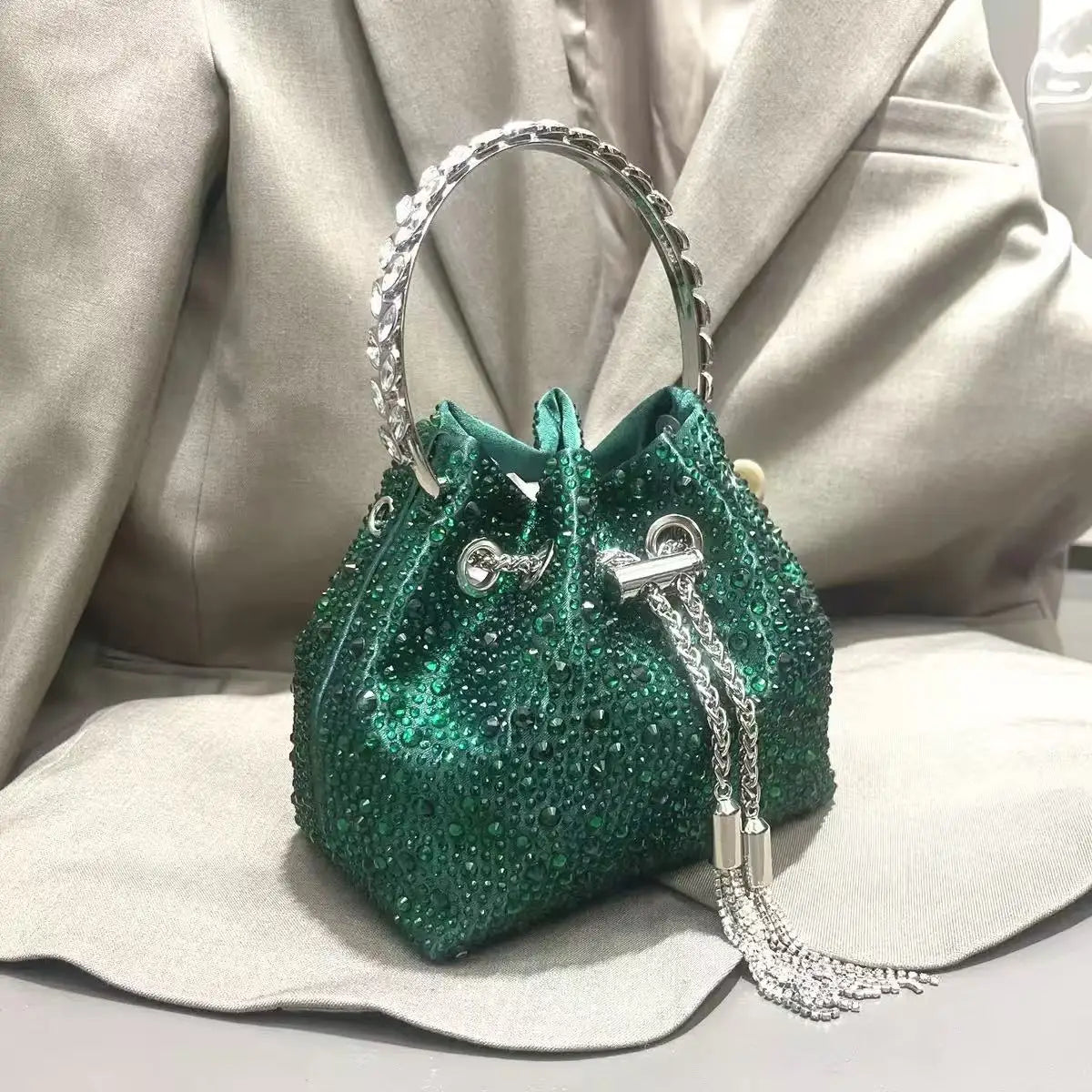 A dark green crystal-embellished evening clutch with a silver chain strap resting on a light fabric surface.