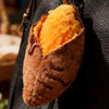 A plush keychain shaped like a roasted sweet potato with orange flesh visible inside.