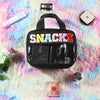 A black clear makeup bag with colorful chenille letters and a waterproof design resting on a pink and blue fuzzy surface.