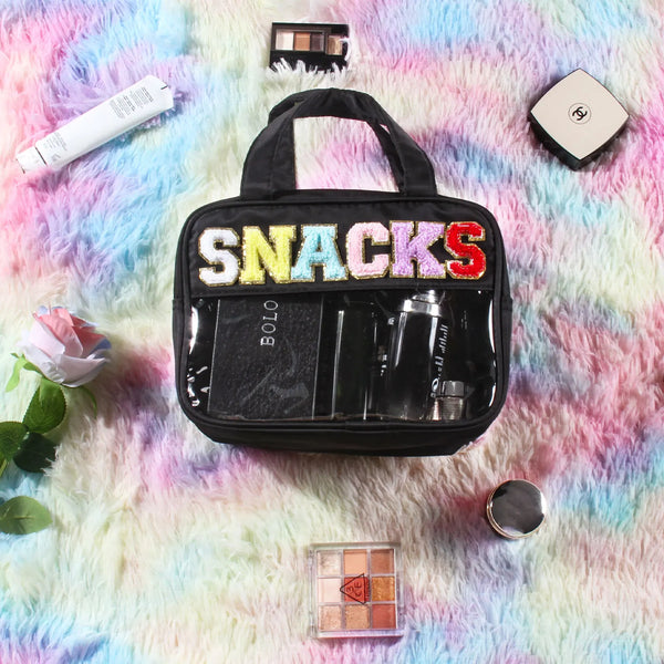 A black clear makeup bag with colorful chenille letters and a waterproof design resting on a pink and blue fuzzy surface.
