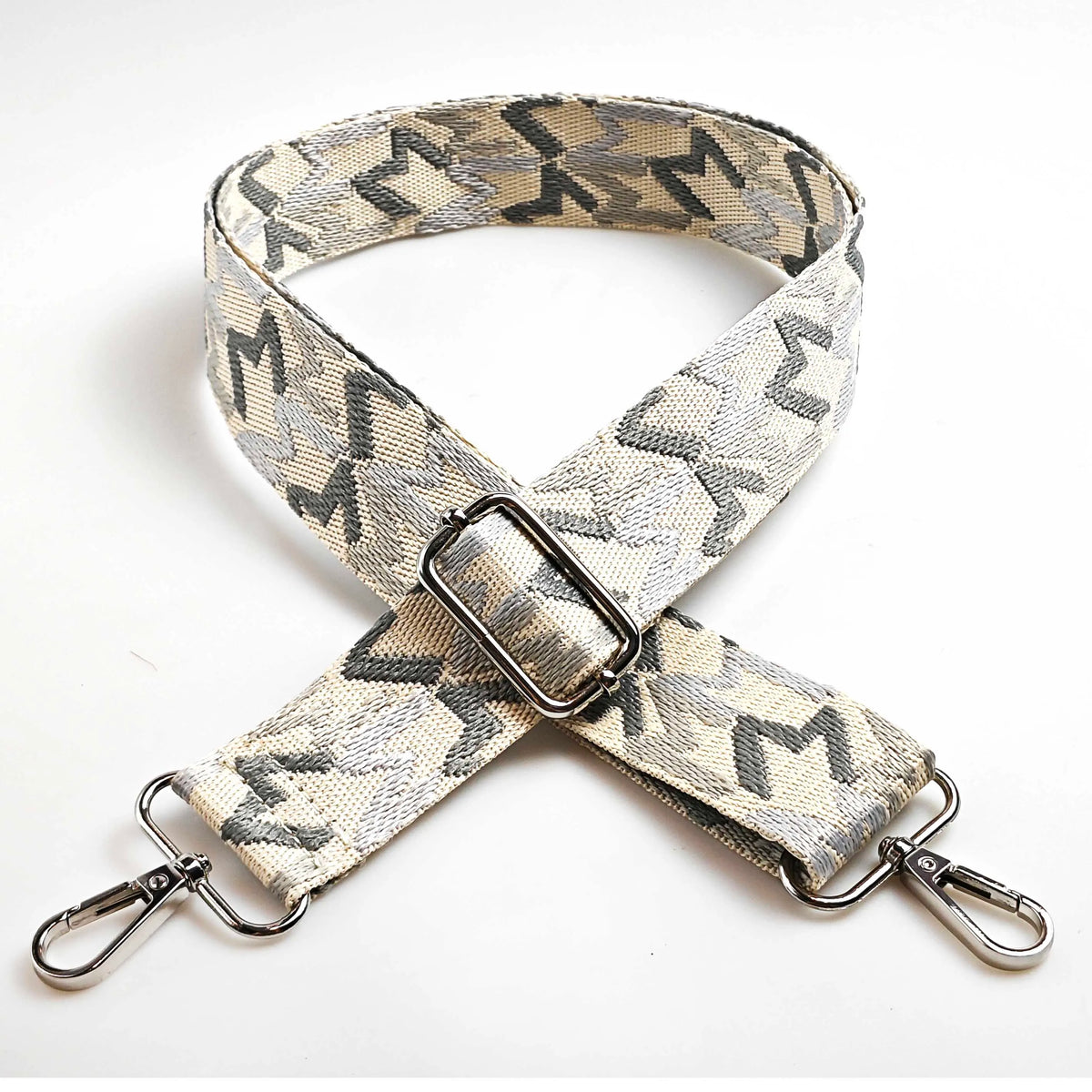 A beige and gray jacquard patterned strap for a crossbody bag featuring an adjustable buckle.