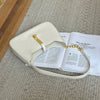 A cream-colored PU leather hobo shoulder bag resting on a beige carpet next to an open book.