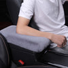 A person is sitting in a car seat with a white shirt, resting their arm on a gray plush car armrest cushion.