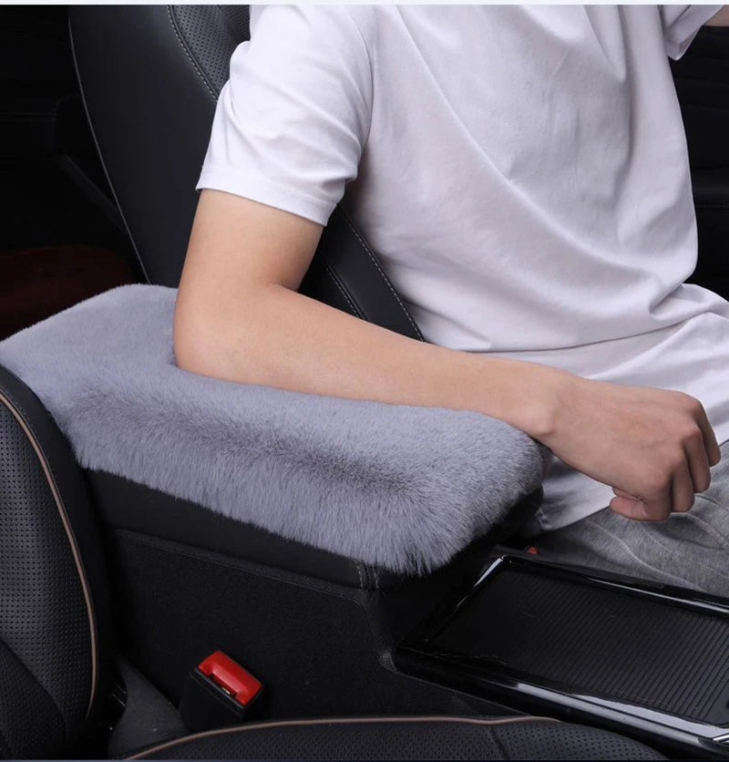 A person is sitting in a car seat with a white shirt, resting their arm on a gray plush car armrest cushion.