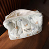 A white quilted cosmetic storage pouch with small printed cats resting on a wooden surface.