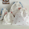 Several white canvas makeup bags with pink and blue bows are displayed on a light surface.
