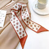 Foulard de soie beige avec motif floral brun et crème, à côté d'un vêtement beige et d'une tasse blanche.