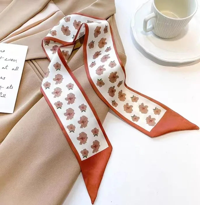 Foulard de soie beige avec motif floral brun et crème, à côté d'un vêtement beige et d'une tasse blanche.