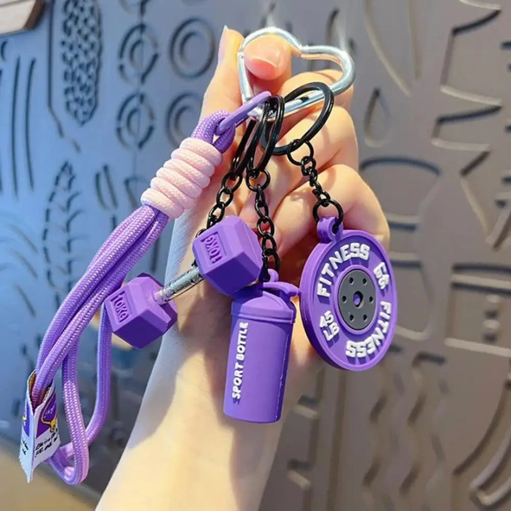 A hand holds a purple fitness keychain featuring a dumbbell and kettlebell charm.