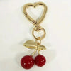 Gold heart-shaped bag charm with a lobster clasp and two red cherry beads.