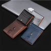 A stack of slim leather wallets in various shades of brown and gray resting on a silver laptop.