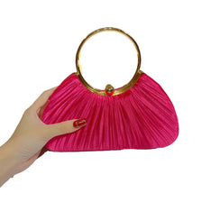 Una mano sostiene un bolso de mano de satén rosa brillante plisado con un ribete dorado.