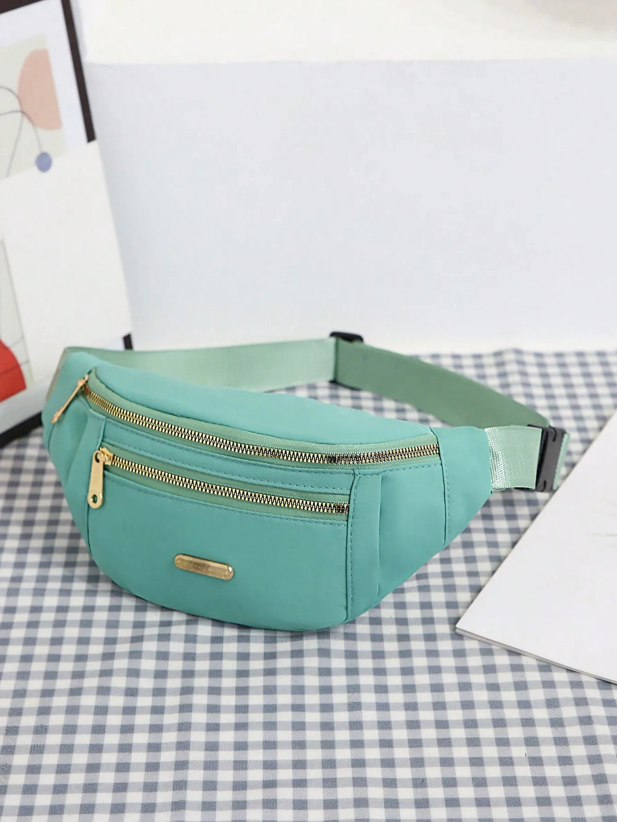 A mint green multi-layer sports waist bag with a zipper and gold accent, resting on a checkered surface.