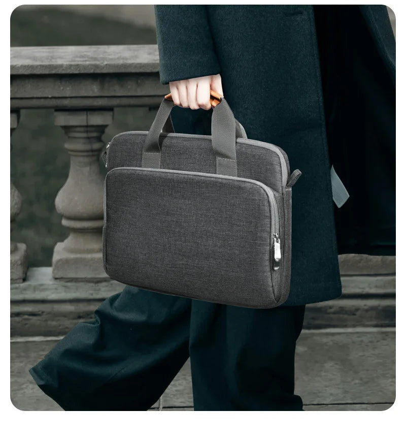 Une personne en costume noir tient une housse de laptop gris foncé et premium.