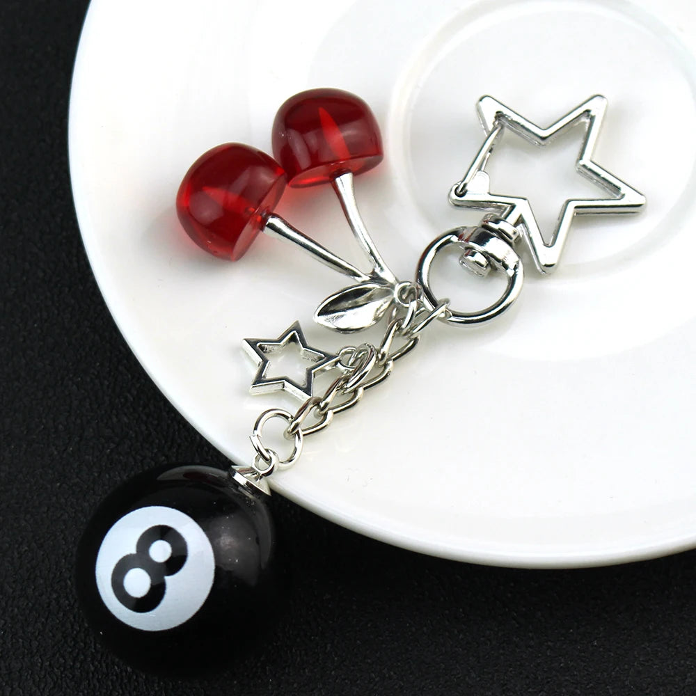 A silver Y2K 8 ball keychain charm featuring a red bead and a black ball on a white plate.