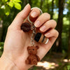 A hand holds a 3D bear pendant keychain made of brown leather and coffee beans.